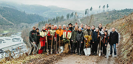 A group of people with gardening tools stand on a rainy forest path