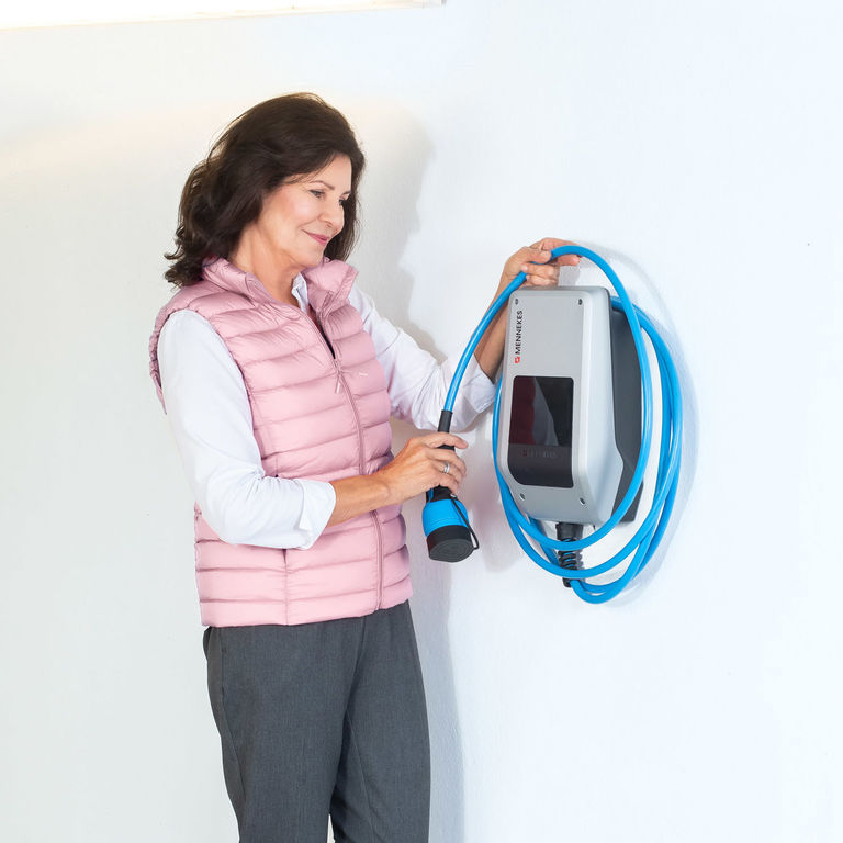  Eine Frau hängt das Ladekabel der Mennekes Wallbox AMTRON® Compact 2.0 in ihrer Garage über die Ladestation.