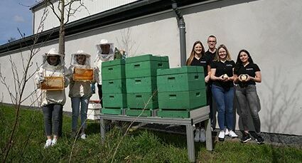Photo of a group of people standing in front of honey houses and holding jars of honey in their hands